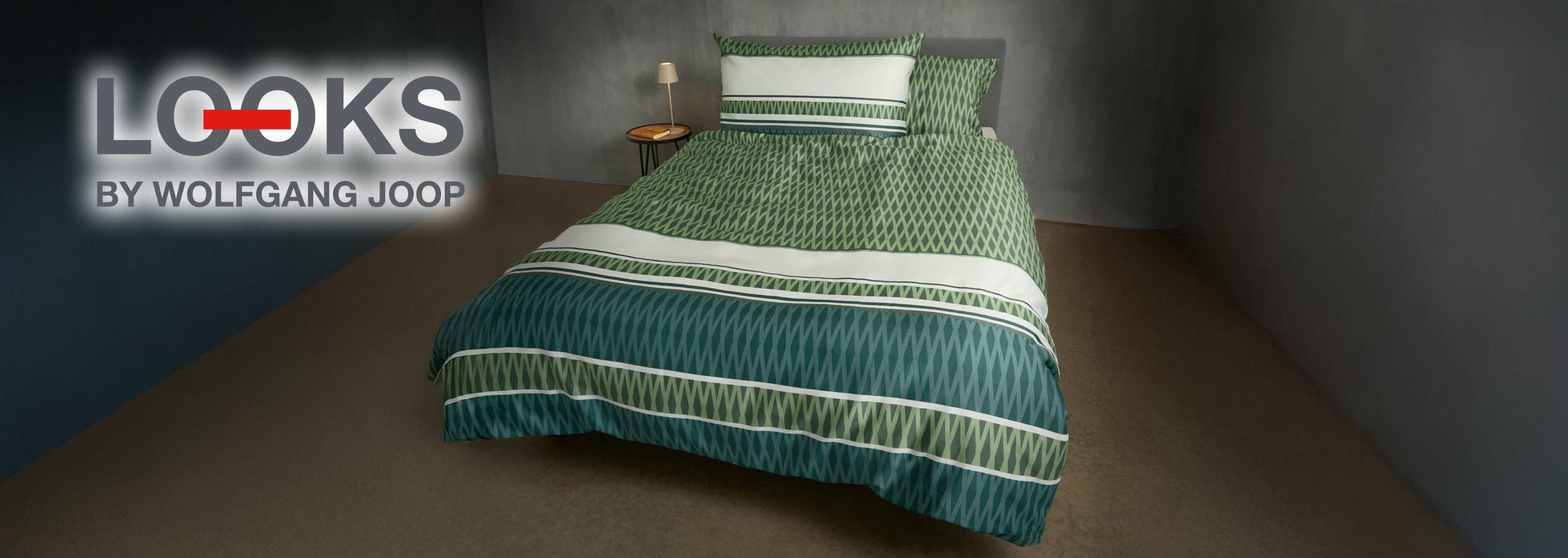 Un letto con biancheria da letto verde e bianca a motivi geometrici, con il logo 'LOOKS BY WOLFGANG JOOP'.