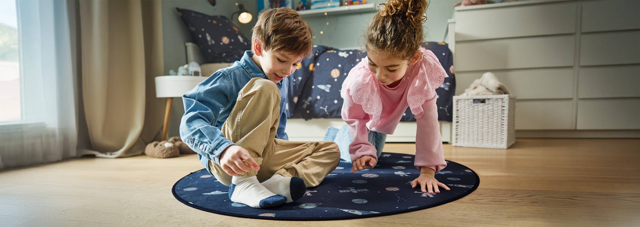 Deux enfants jouent sur un tapis rond à thème spatial.