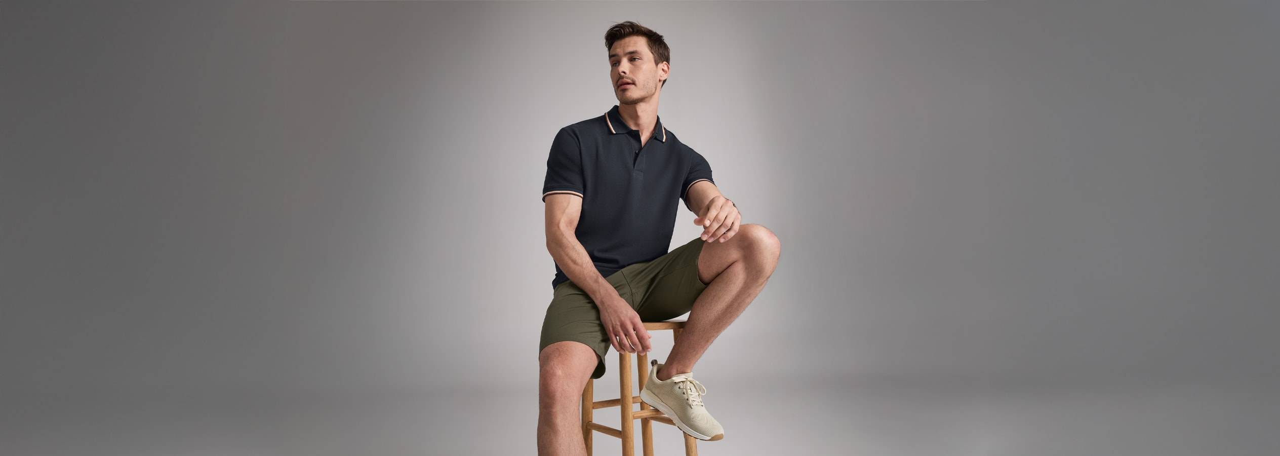 Un uomo elegante indossa una polo nera e pantaloncini kaki.