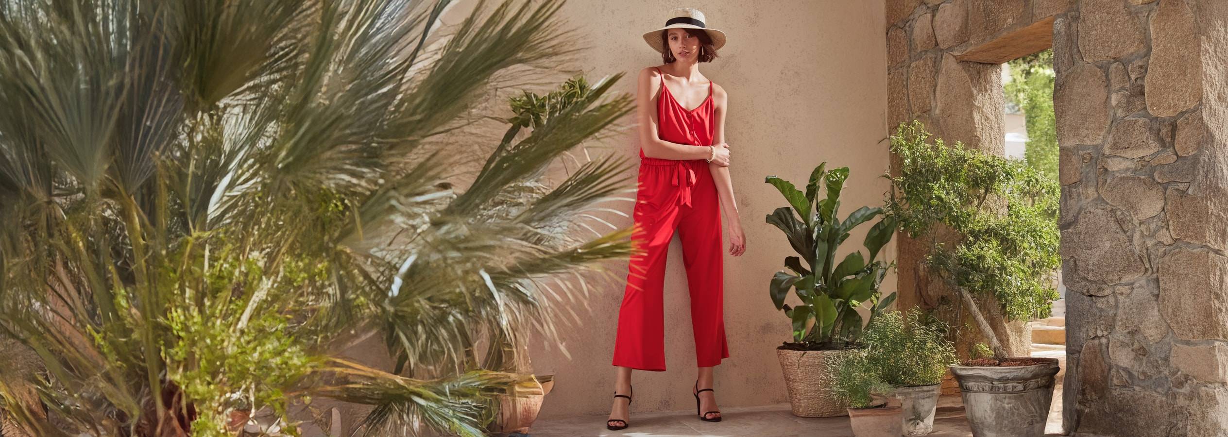 Eine Frau trägt einen eleganten roten Jumpsuit in einer mediterranen Außenumgebung.