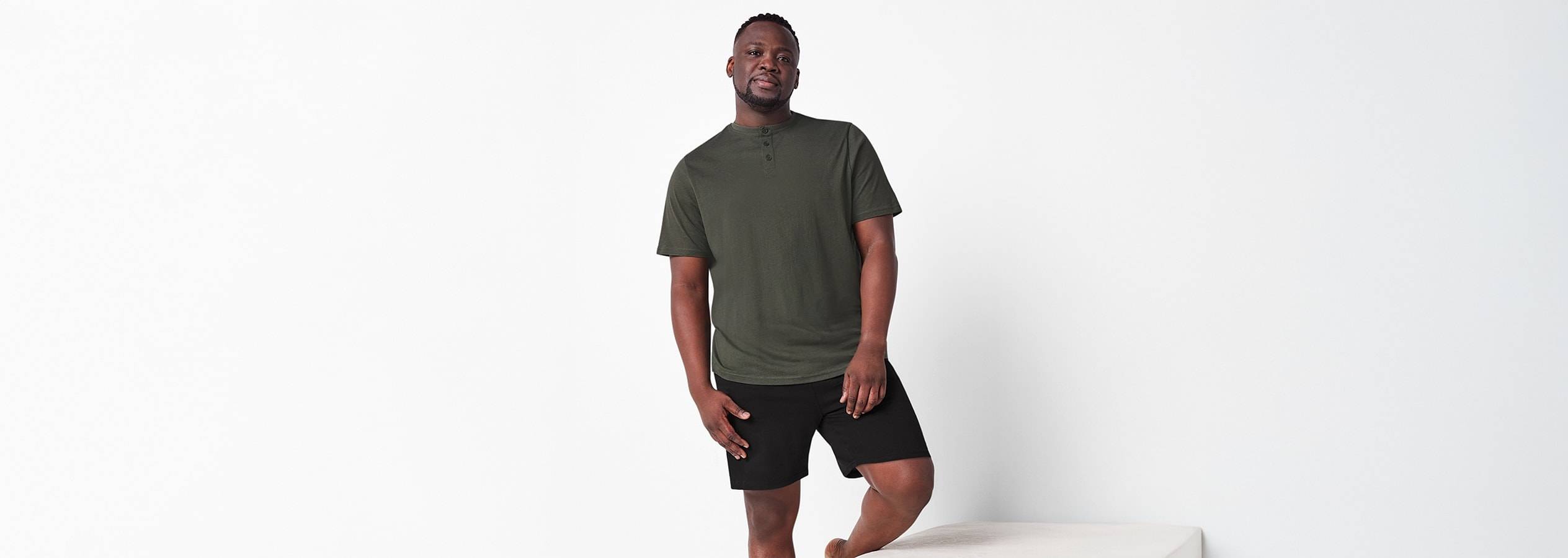 Un homme porte un t-shirt henley vert olive et un short noir.