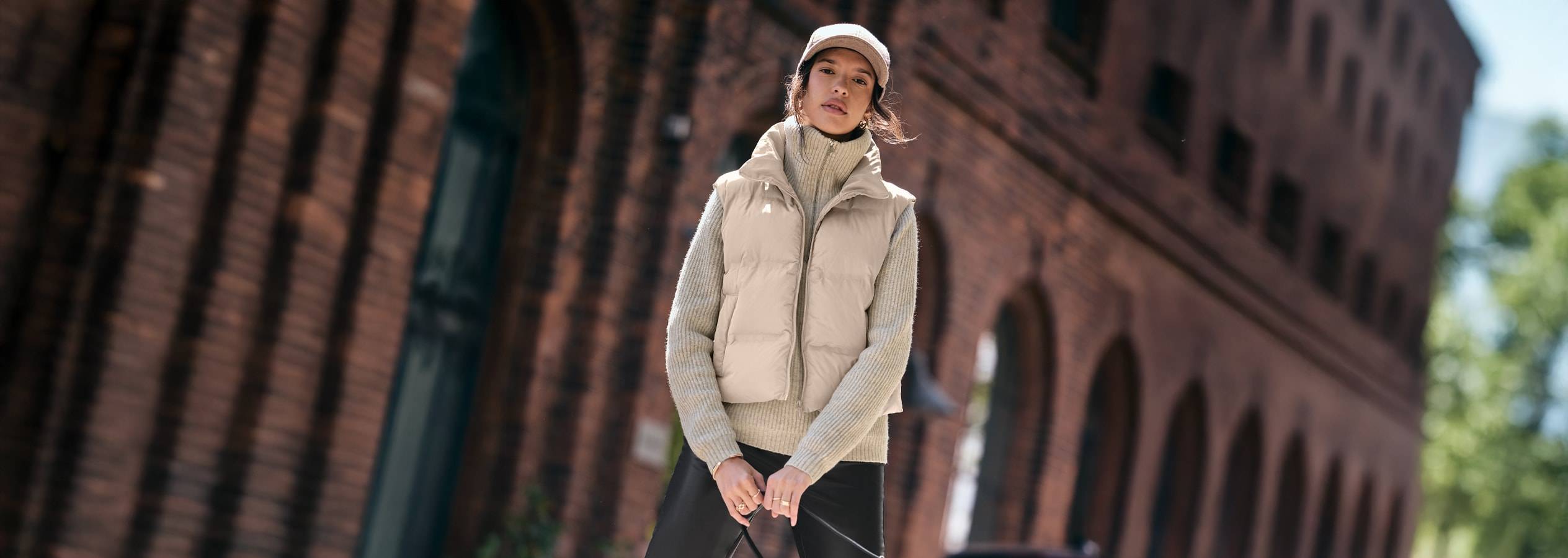 Donna in gilet imbottito beige, maglione a collo alto e pantaloni neri in città.