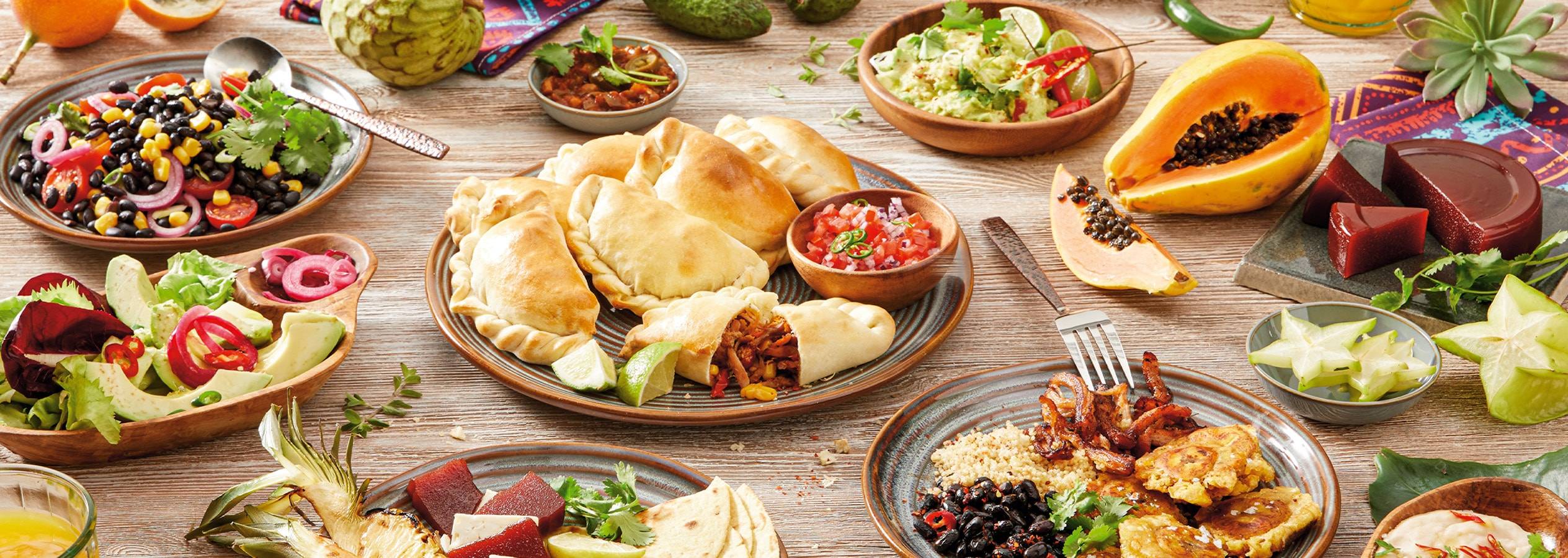 Ein Holztisch mit Empanadas, Salaten, Früchten und Saucen.
