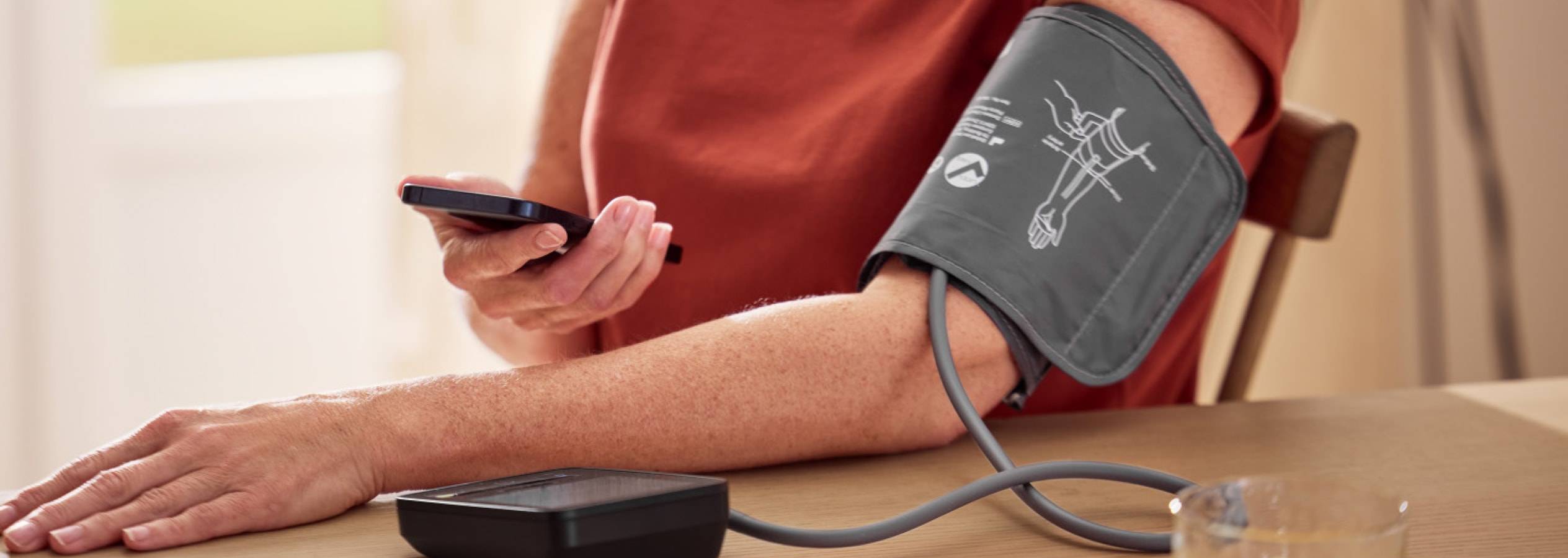 Eine Person benutzt ein Blutdruckmessgerät und ein Smartphone.