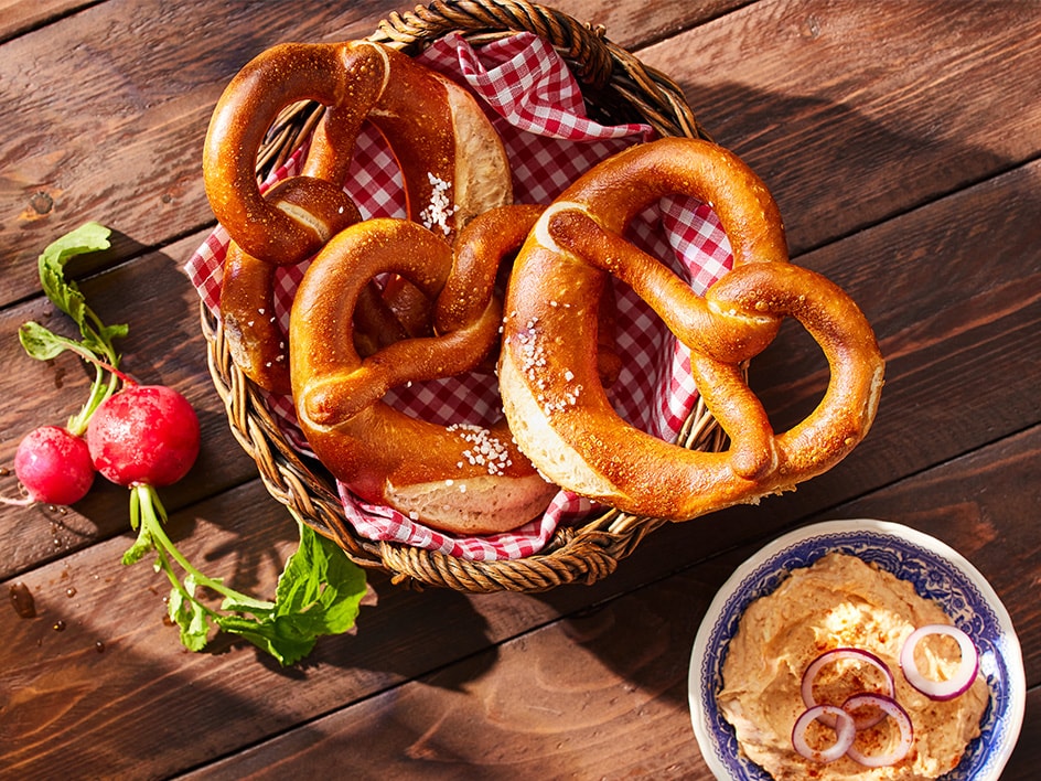 Brezeln in einem Korb mit Radieschen und einem Dip auf einem Holztisch.