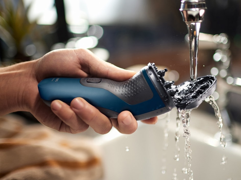 Une main lave un rasoir électrique Braun sous l'eau courante.