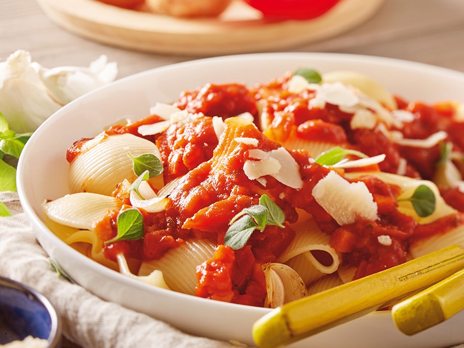 Eine Schüssel mit Muschel-Pasta in Tomatensauce, garniert mit Parmesan und frischen Kräutern.