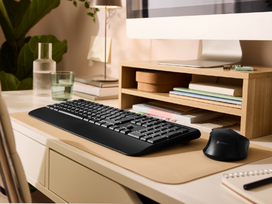 Schreibtisch mit Tastatur, Maus, Monitor und Holzregal.