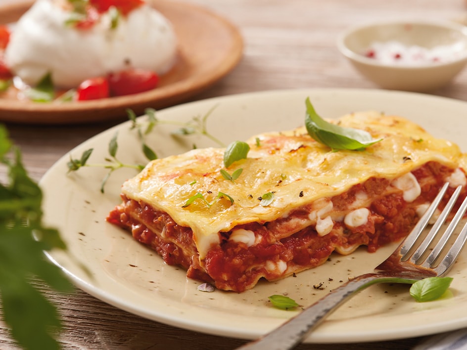 Ein Stück Lasagne auf einem Teller, garniert mit Basilikum.