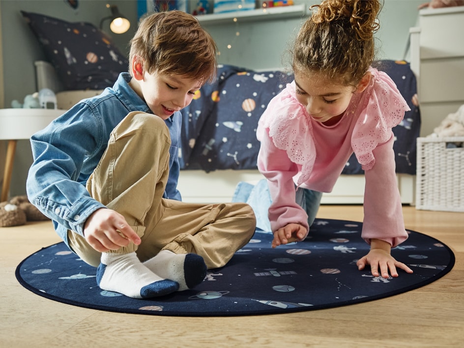 Deux enfants jouent sur un tapis rond à thème spatial.