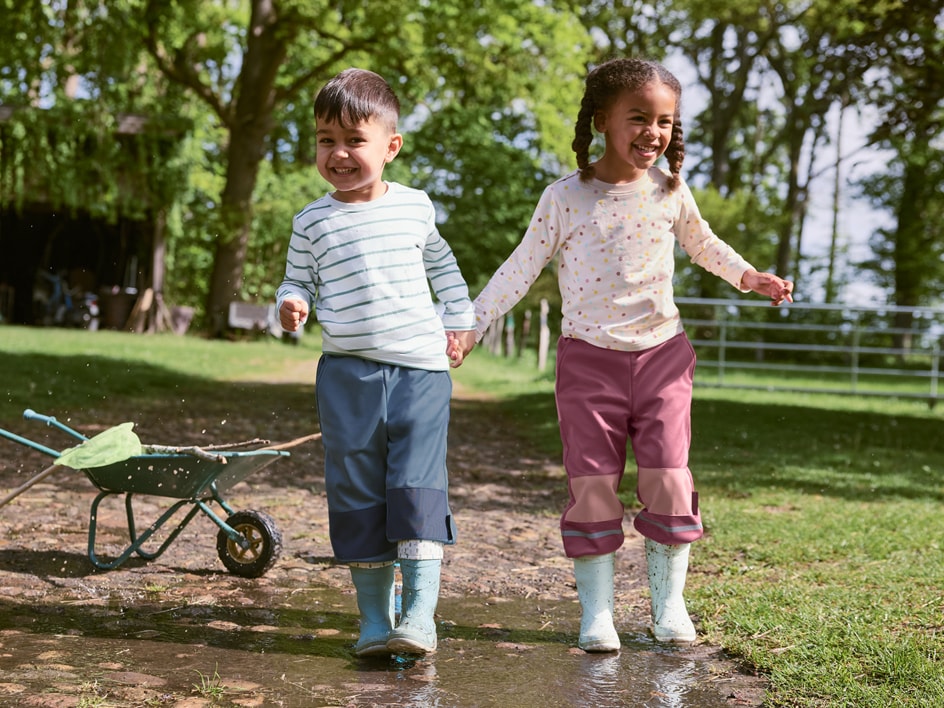 Deux enfants jouent dans la boue avec des bottes en caoutchouc et des pantalons imperméables.