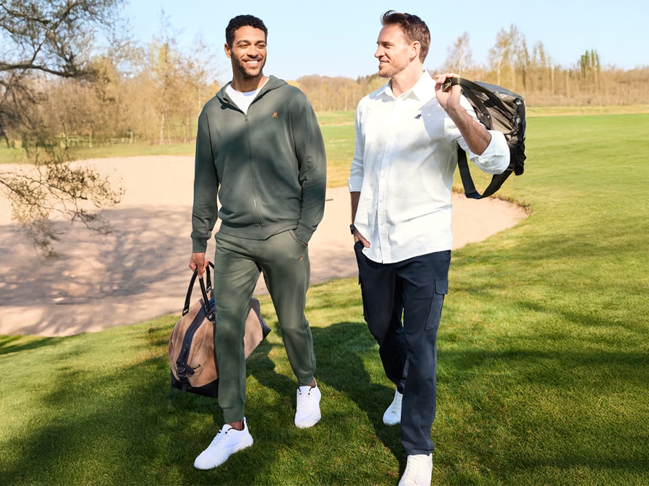 Zwei Männer in Freizeitkleidung gehen über einen Golfplatz.