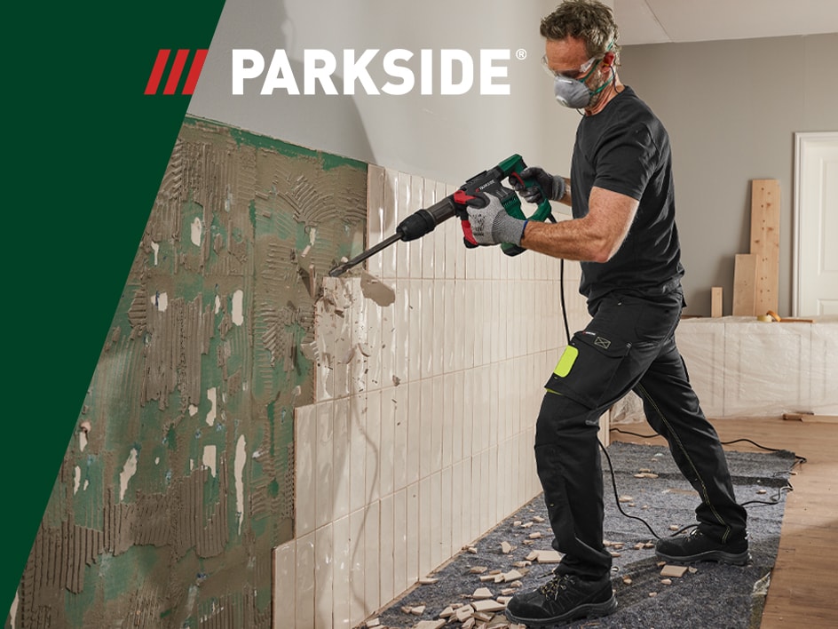 Ein Mann verwendet einen Parkside-Abbruchhammer, um Fliesen von einer Wand zu entfernen.