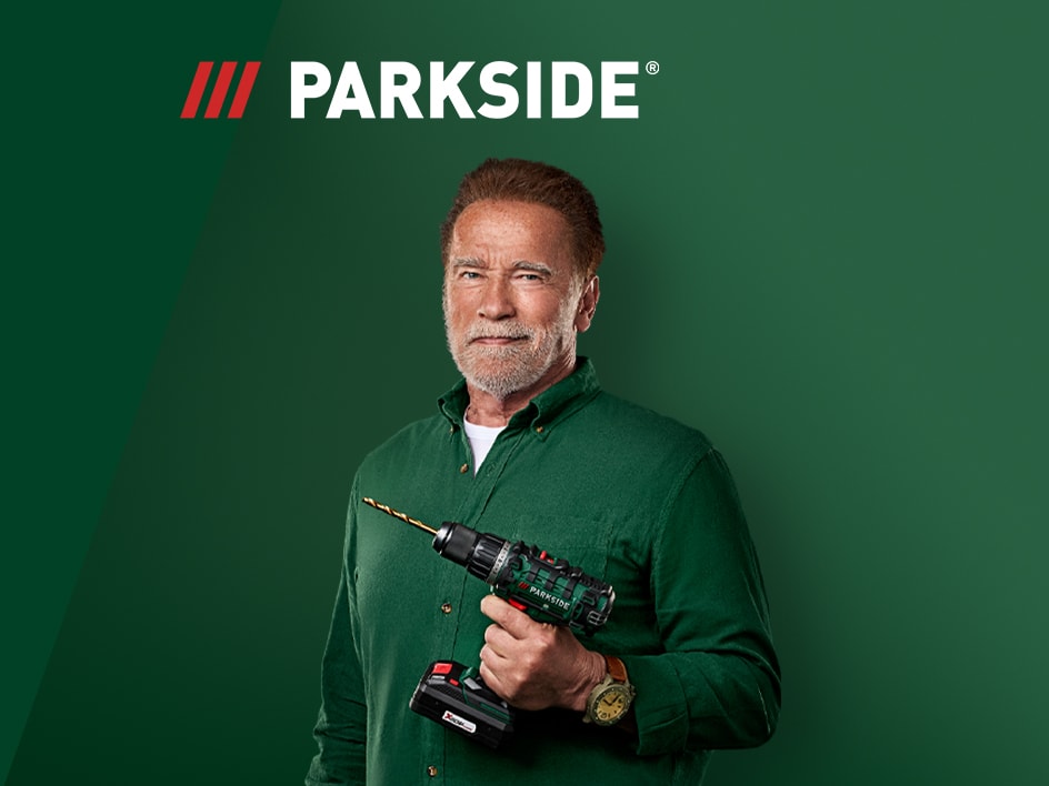 Arnold Schwarzenegger hält einen Parkside Akku-Bohrschrauber vor grünem Hintergrund.
