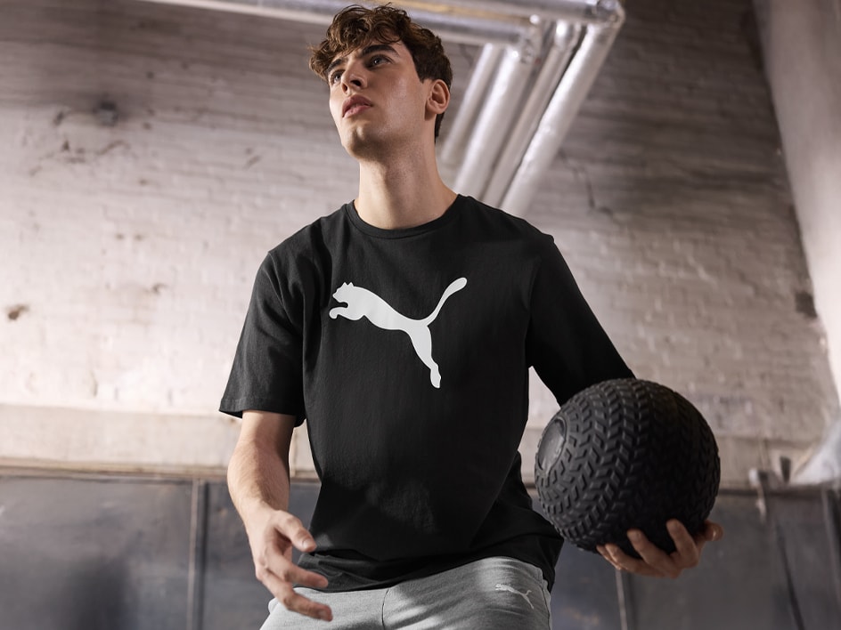Ein Mann trägt ein schwarzes Puma-T-Shirt und hält einen Medizinball.