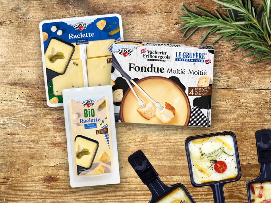 Packungen mit Raclette- und Fonduekäse auf einem Holztisch, mit Raclettepfännchen.