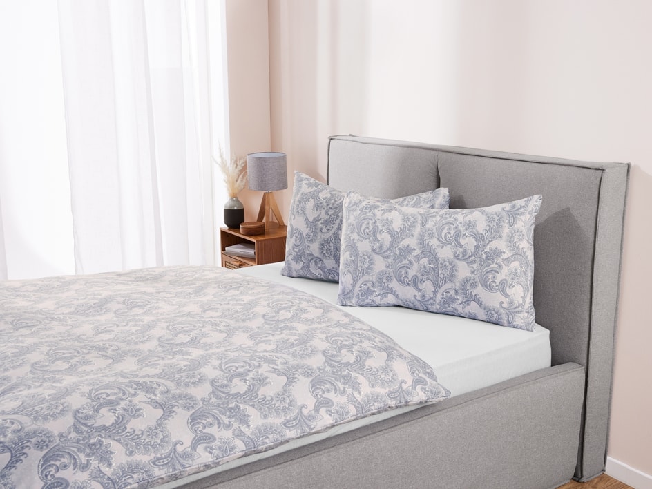 Un letto grigio con biancheria da letto a fantasia paisley blu e bianca in una camera luminosa.