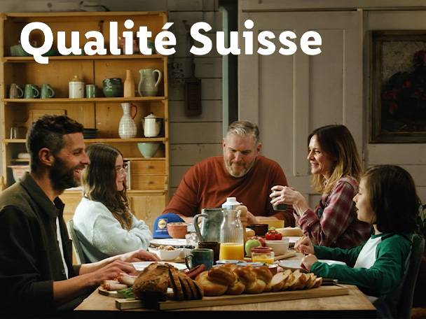 Familie am Tisch mit Brot und Orangensaft, Text: Qualité Suisse.