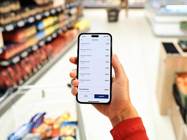 Hand hält Smartphone mit Einkaufs-App in einem Supermarkt.