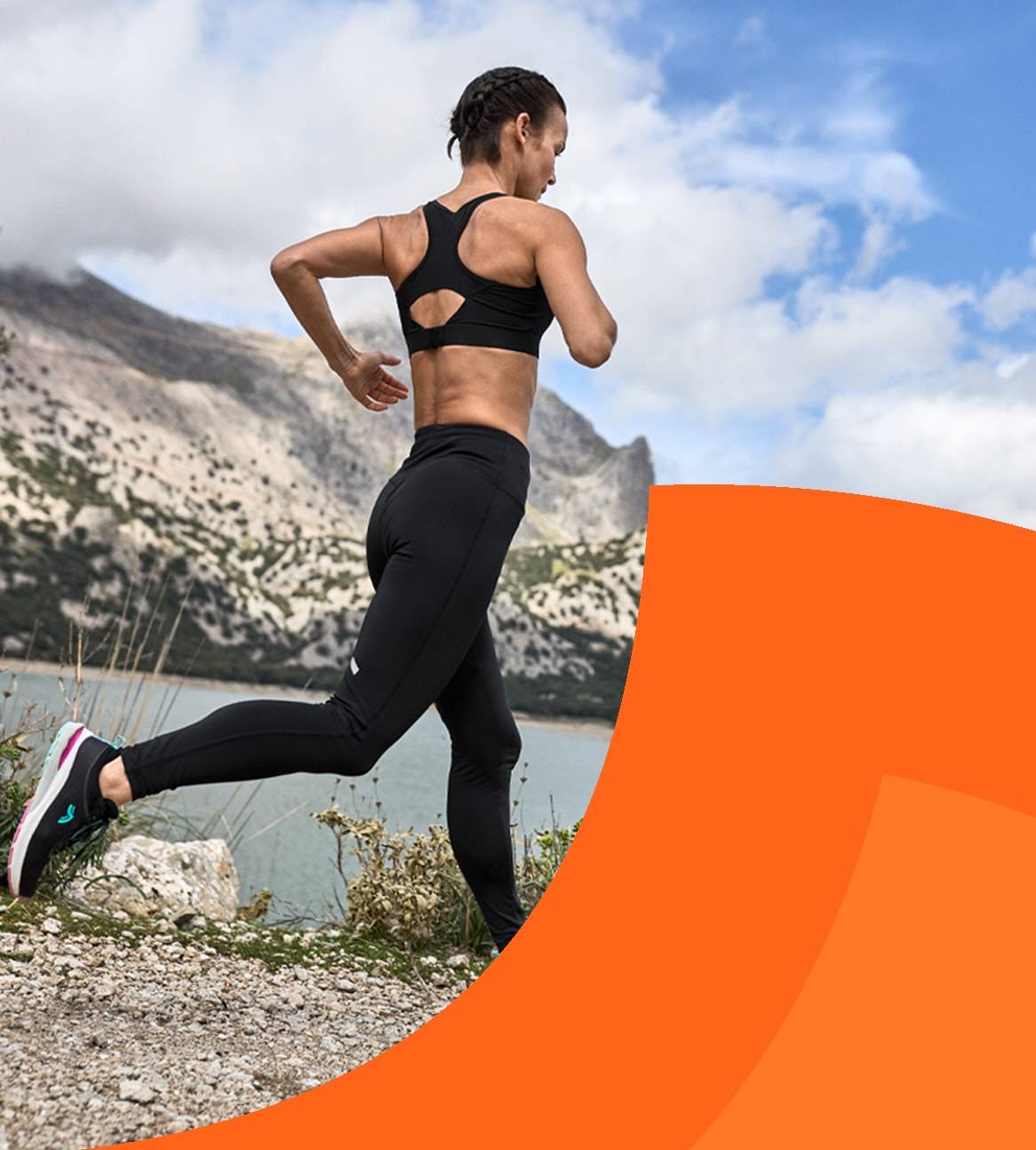 Donna in abbigliamento sportivo nero corre su un sentiero di montagna.
