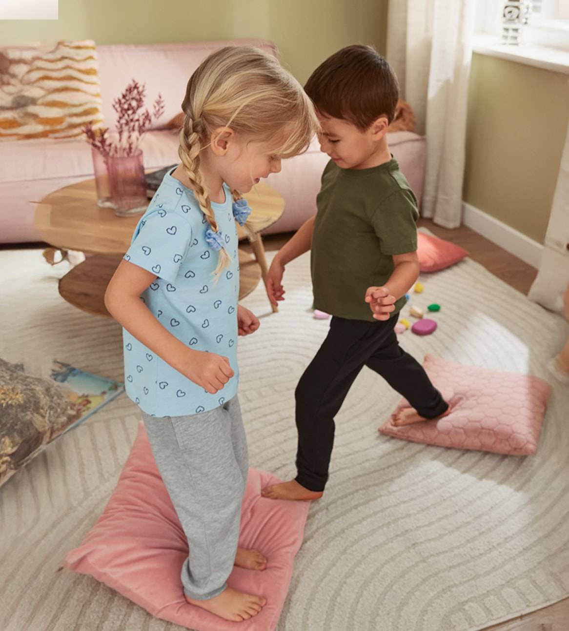 Deux enfants jouent sur des coussins, portant des vêtements à motifs cœurs.