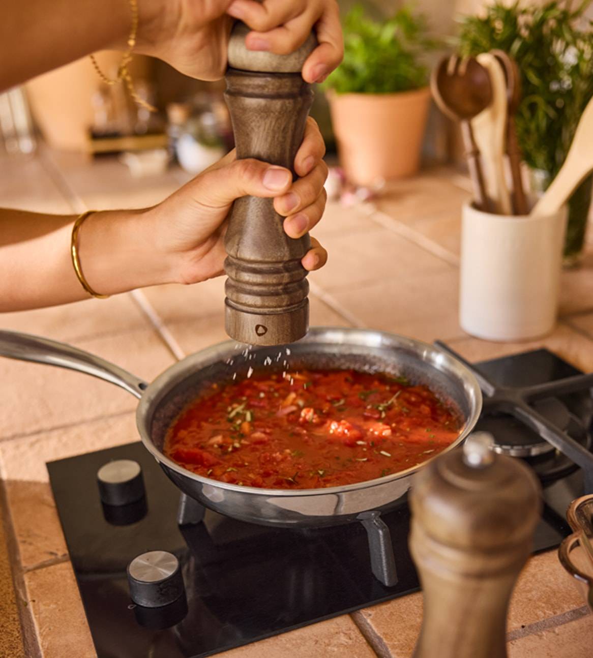 Eine Person würzt eine Tomatensauce in einer Pfanne mit einem Pfeffermühle.