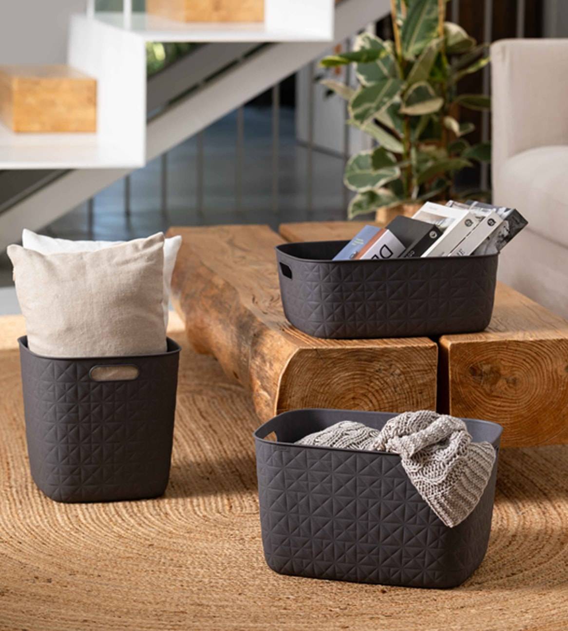 Tre cesti portaoggetti grigi con motivo geometrico, uno con cuscini, uno con libri e uno con una coperta.