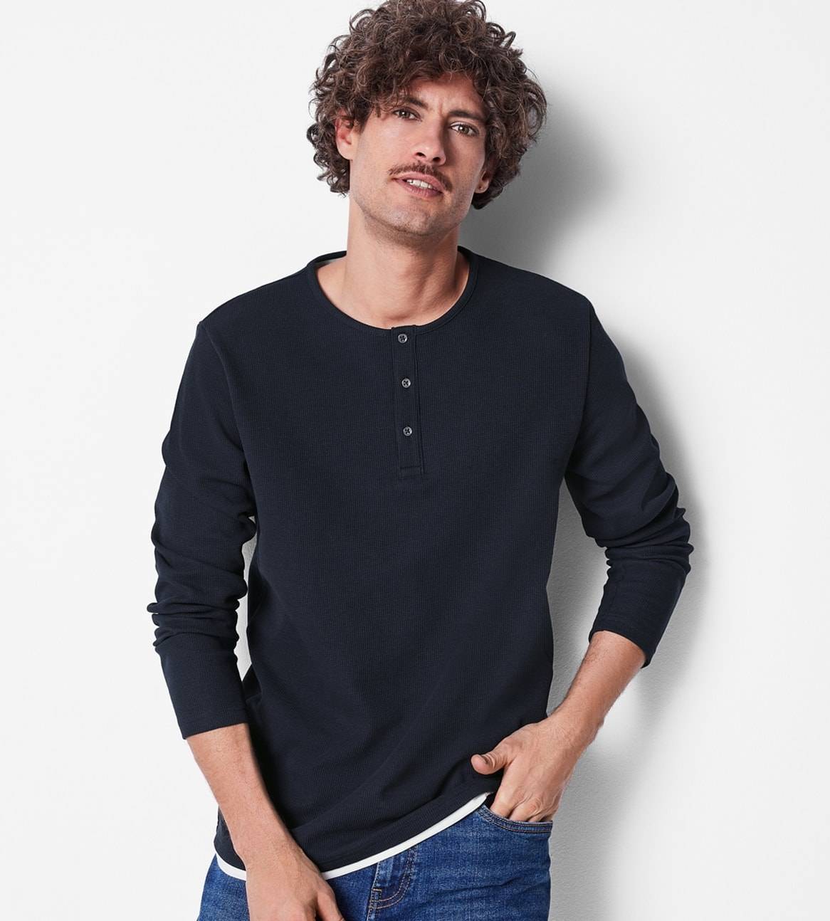 Ein Mann in einem dunkelblauen Henley-Shirt und Jeans.