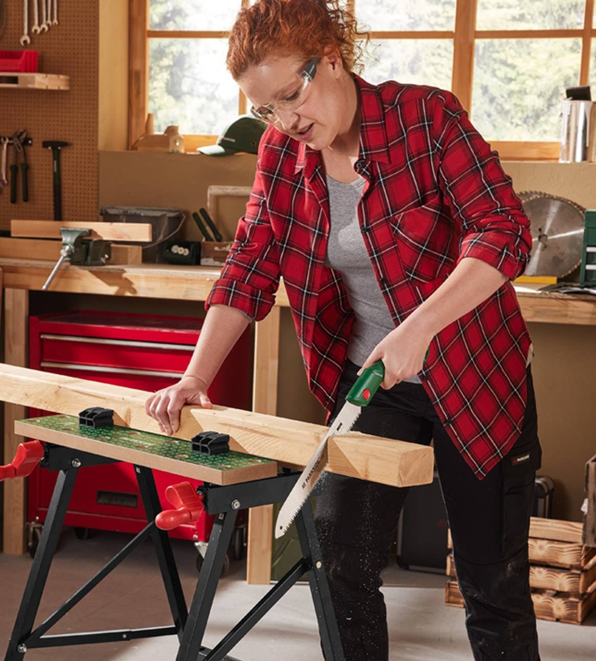 Une femme dans un atelier utilise une scie à main pour couper une poutre en bois sur un établi.