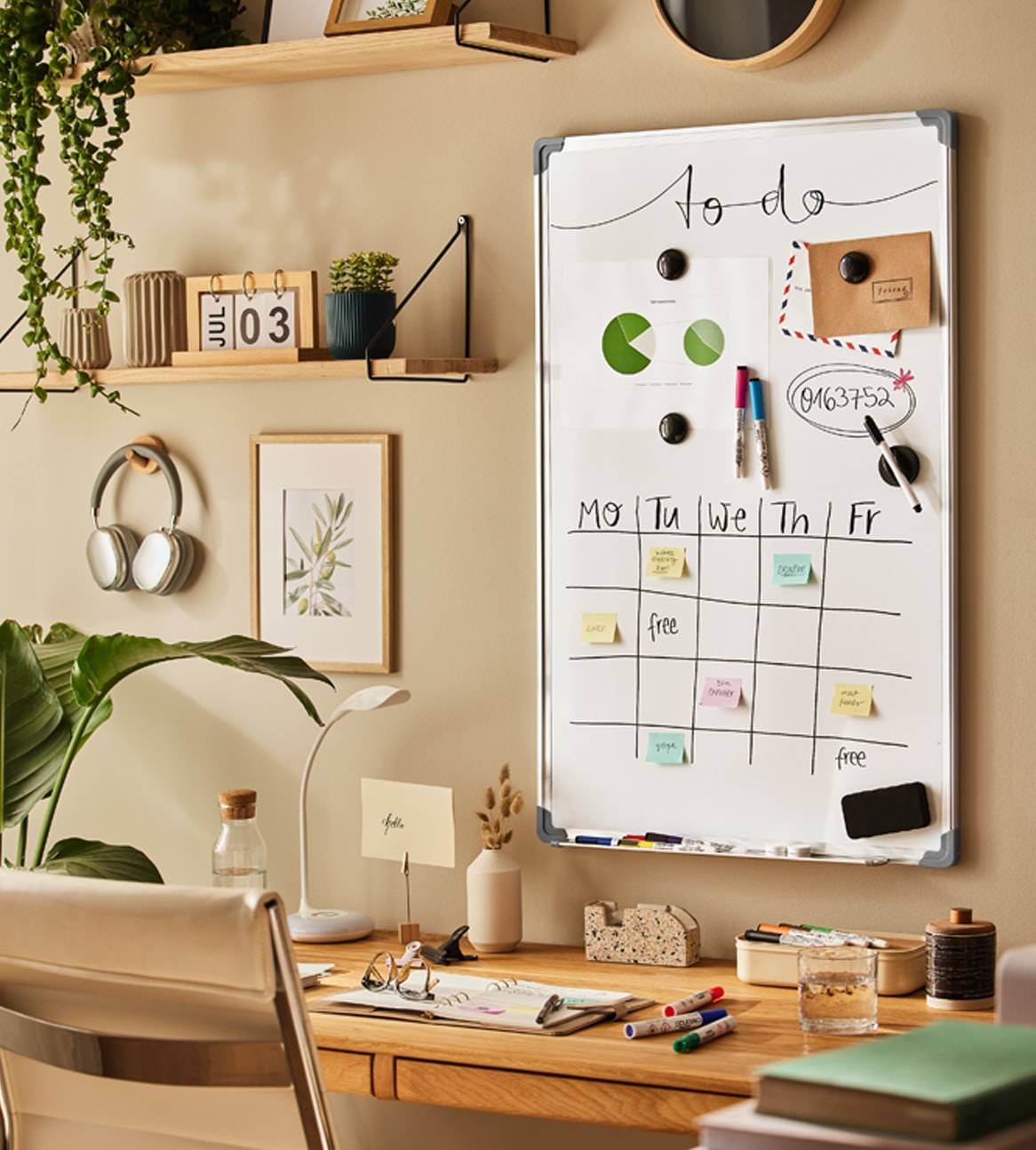 Ein weißes Trockenlöschboard mit Wochenplaner und To-Do-Liste an einem hellen Schreibtisch mit Pflanzen und Bürobedarf.