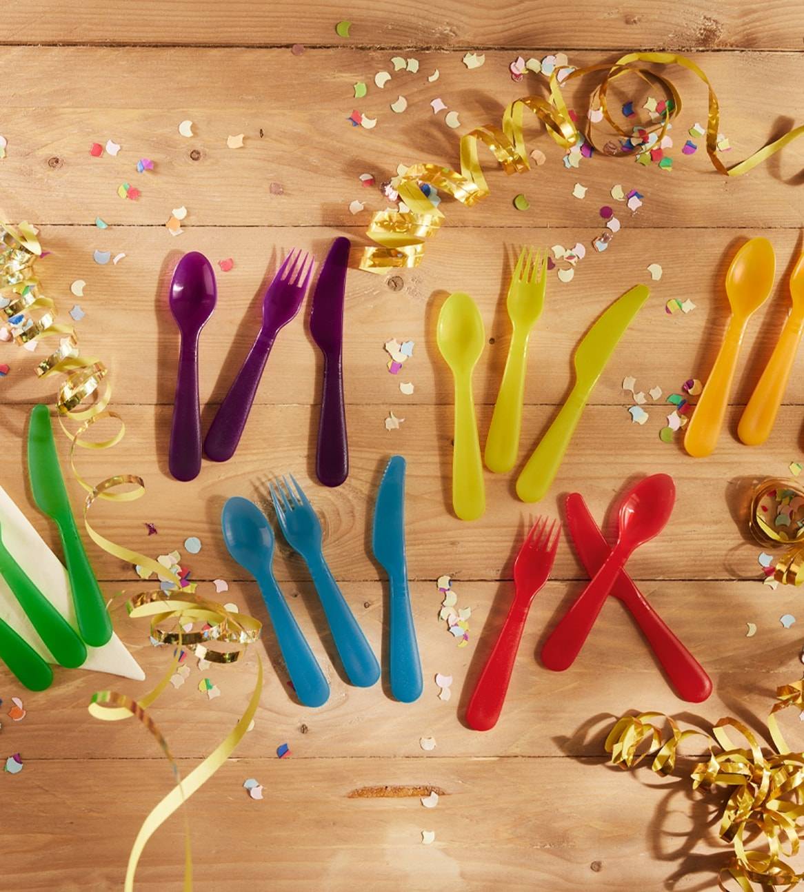 Buntfarbige Plastikbesteck auf Holztisch mit Konfetti.