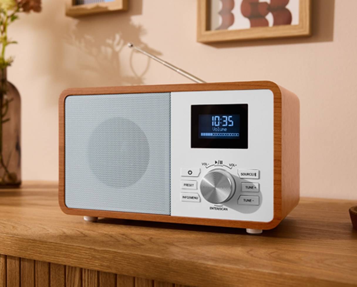 Ein digitales Radio aus Holz und Weiß mit Display und Bedienelementen auf einem Holztisch.