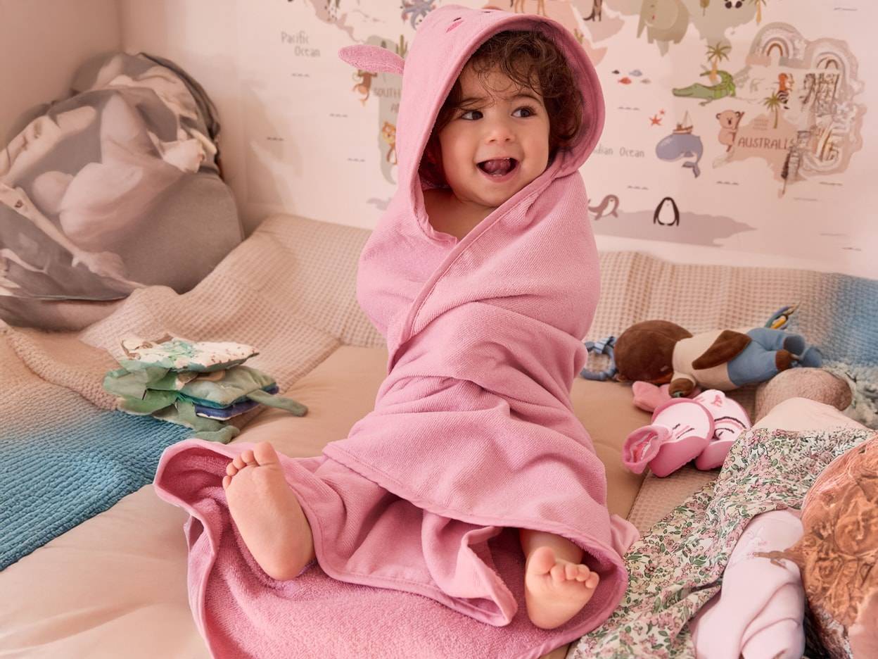 Un bambino carino avvolto in un tenero asciugamano rosa a forma di coniglio dopo il bagno.