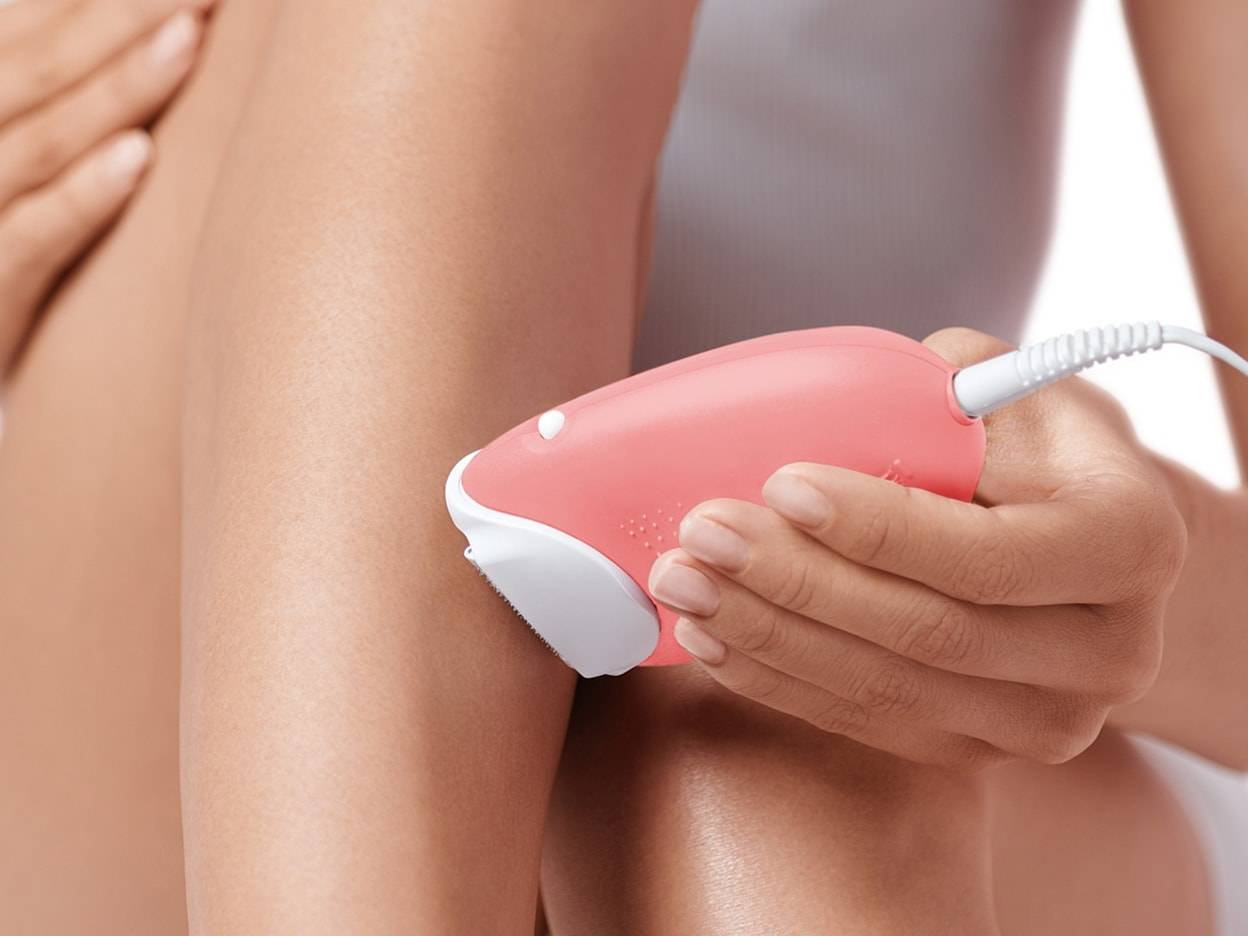 Une femme utilise un épilateur rose sur sa jambe.