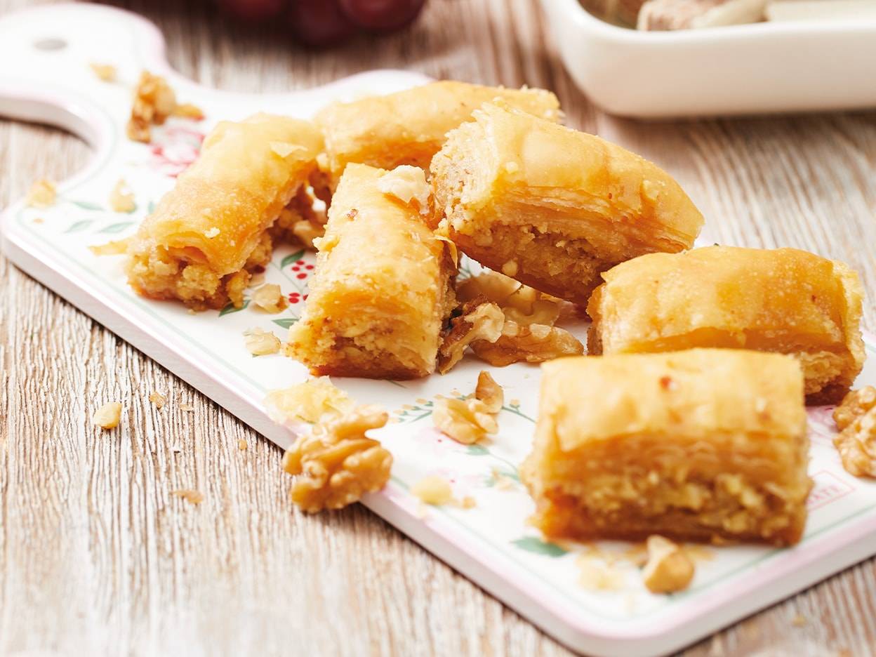 Baklava dorée et noix éparpillées sur une planche à découper décorée.
