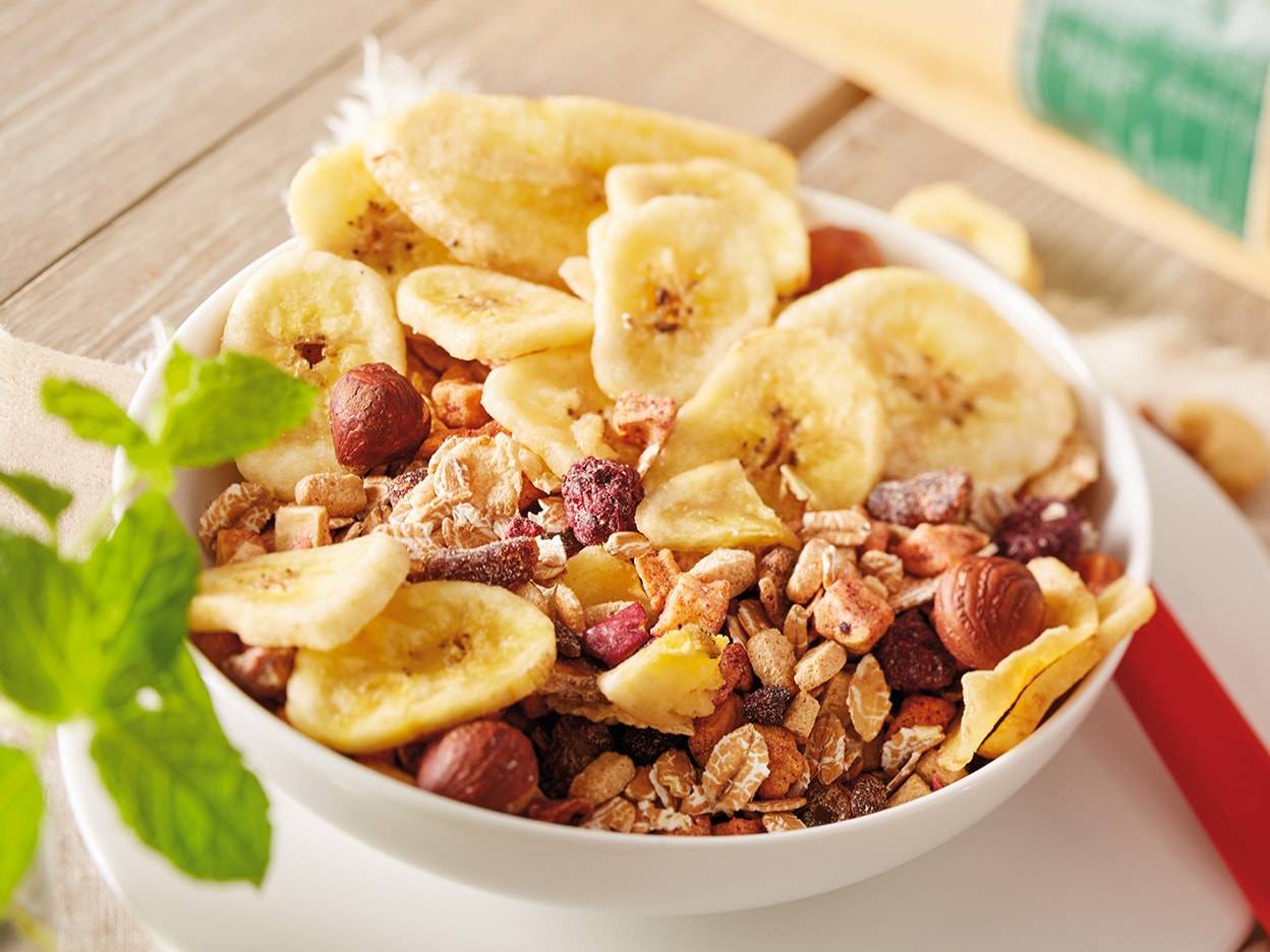 Schale mit Müsli, getrockneten Bananen und Haselnüssen.