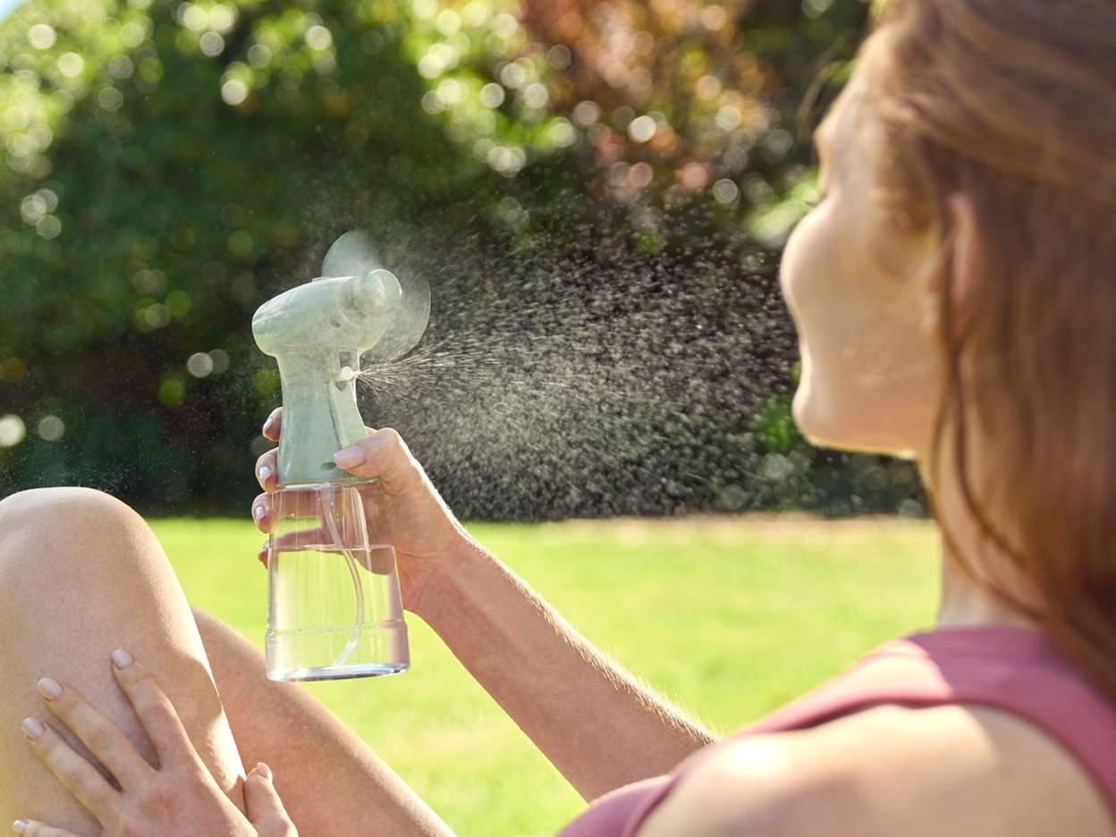 Eine Frau erfrischt sich an einem sonnigen Tag mit einem tragbaren Sprühventilator im Freien.