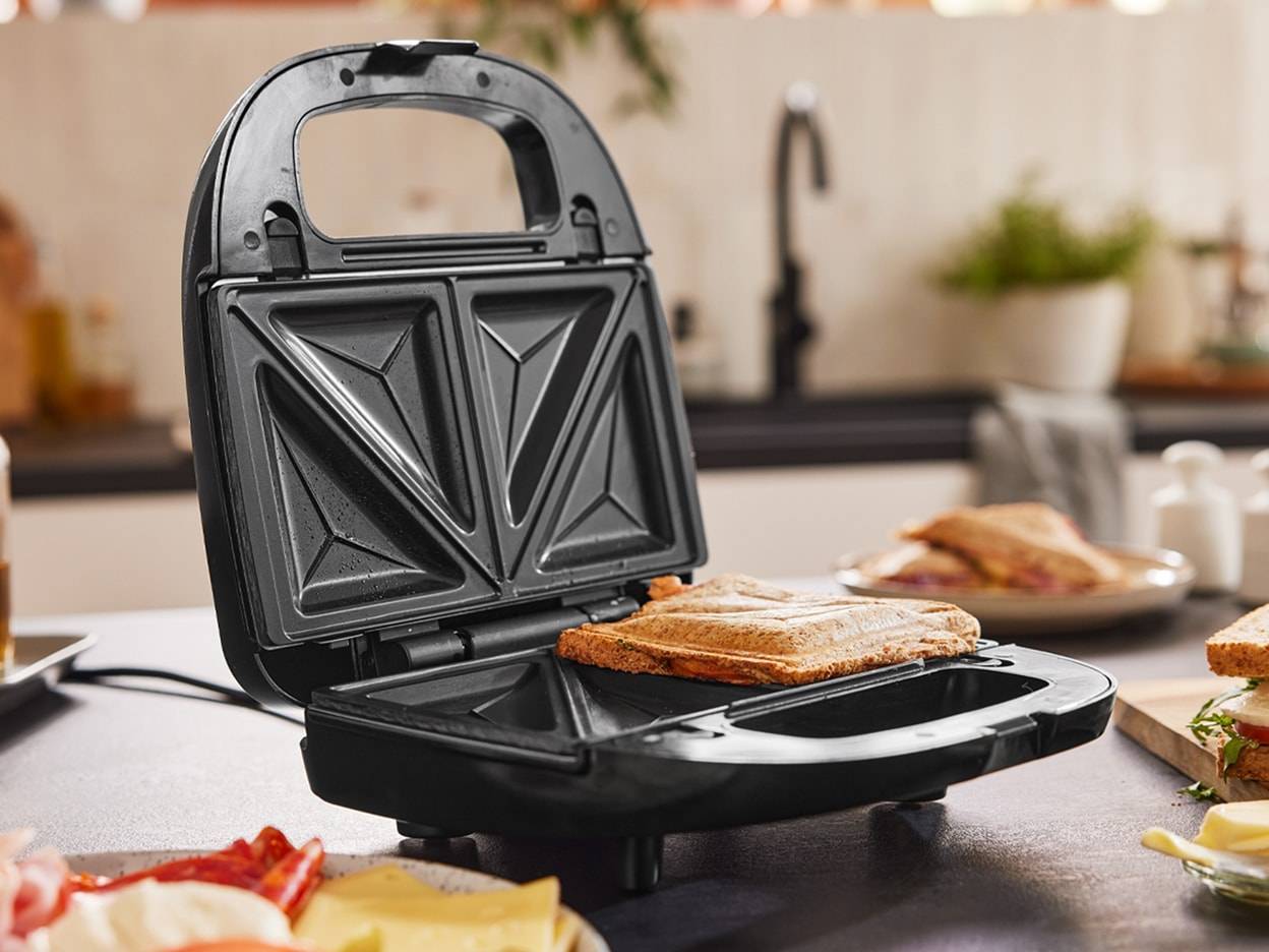 Un tostapane nero aperto con un panino all'interno, su un piano cucina.