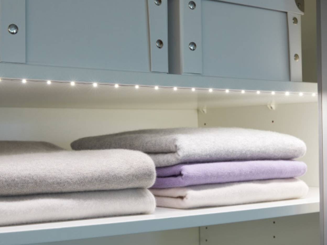 Gefaltete Pullover auf einem Regal, beleuchtet von LED-Lichtern in einem Schrank.