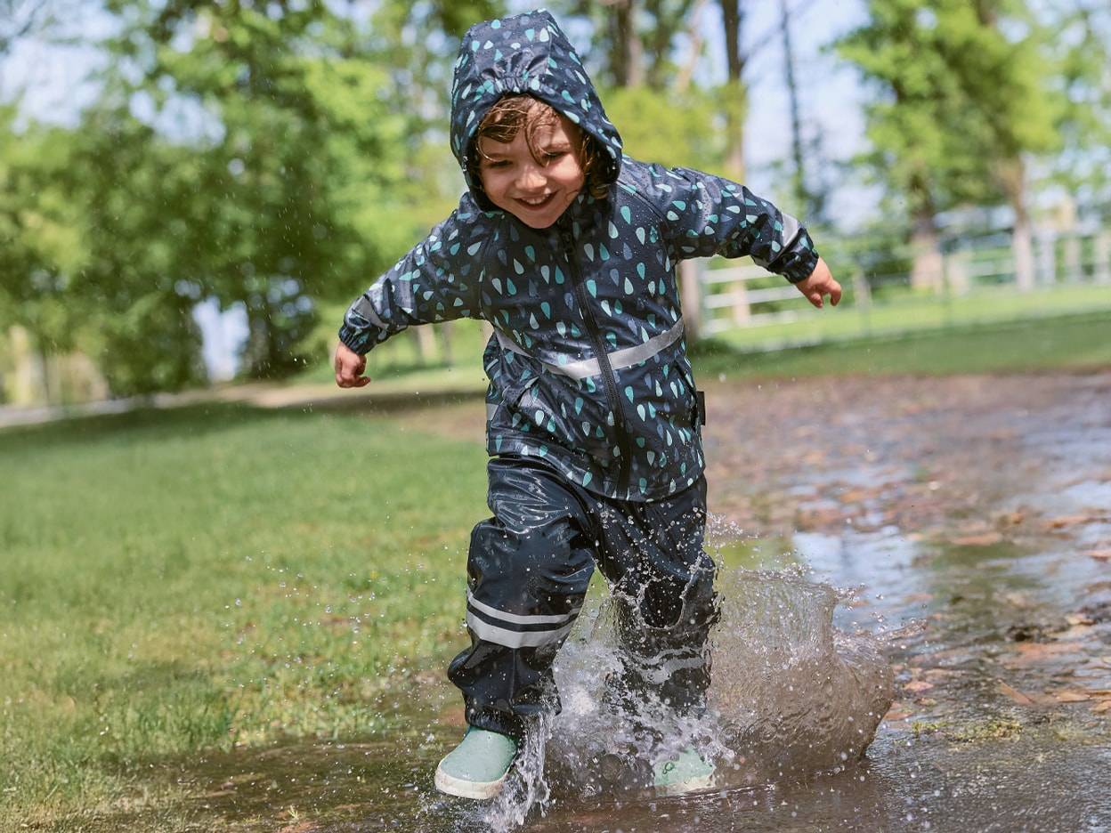 Un enfant joyeux en combinaison de pluie et bottes saute dans une flaque d'eau.