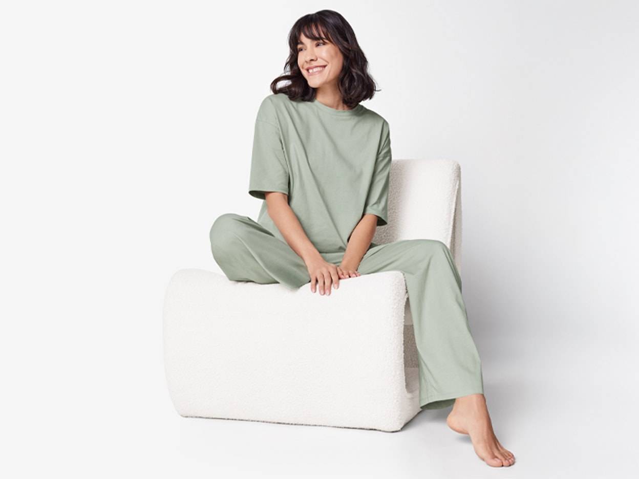 Femme souriante en pyjama vert menthe assise sur un fauteuil blanc.