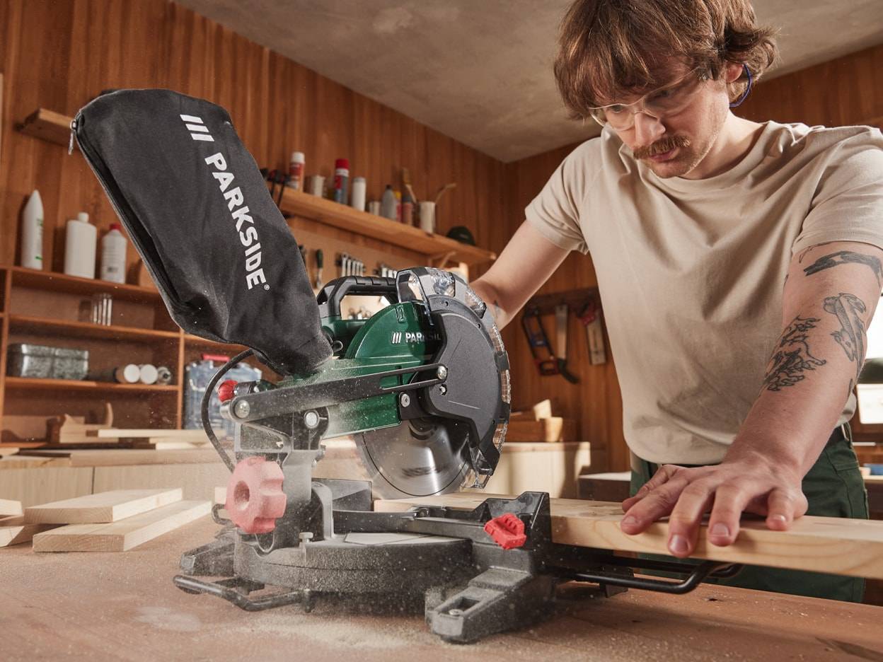 Ein Mann verwendet eine Parkside-Kapp- und Gehrungssäge, um Holz in seiner Werkstatt zu schneiden.