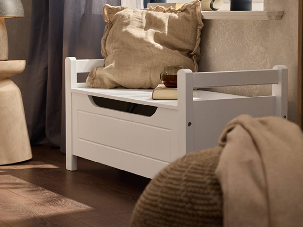Panca contenitore bianca con cuscino beige e plaid in un soggiorno.