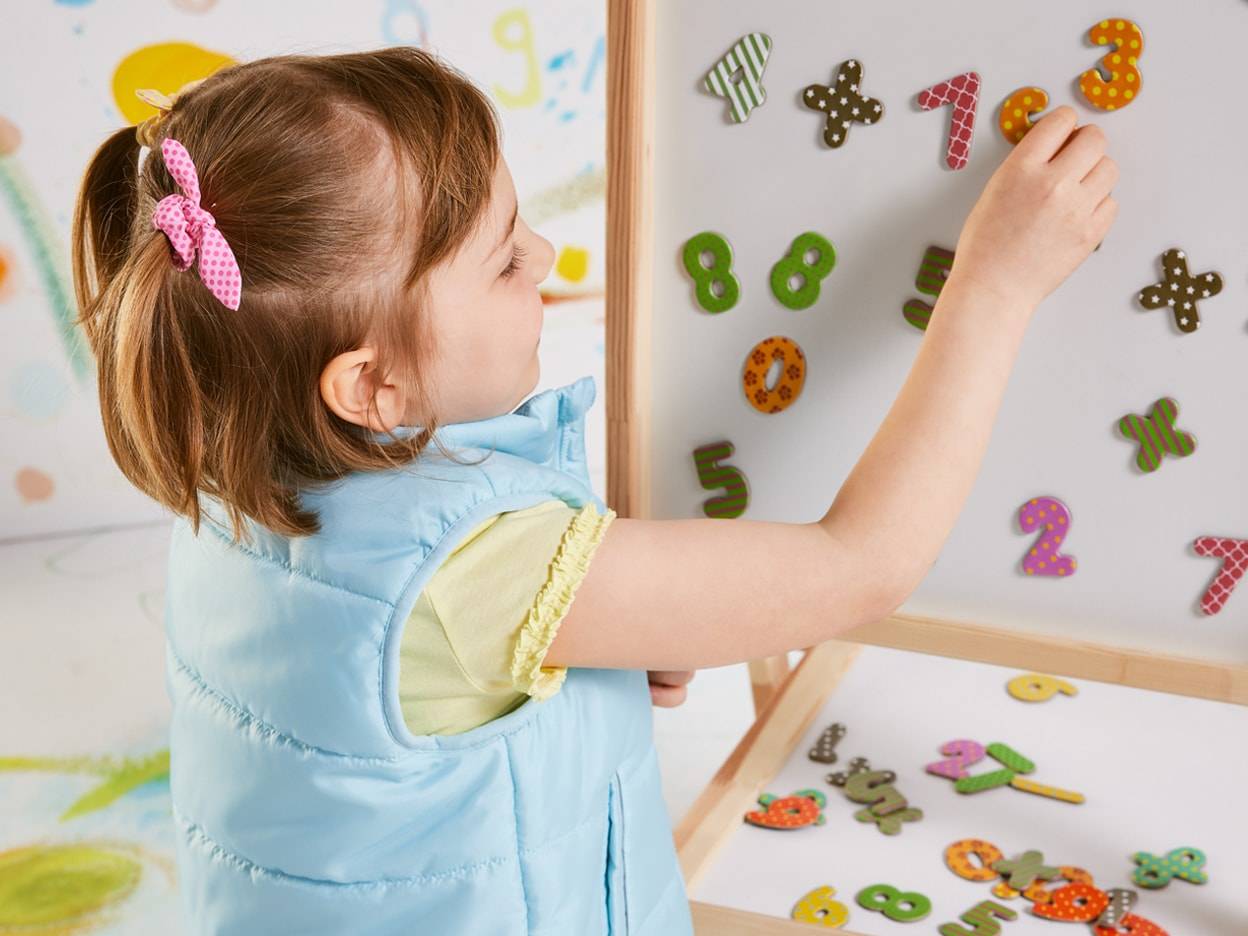 Una bambina gioca con numeri magnetici su una lavagna per imparare.