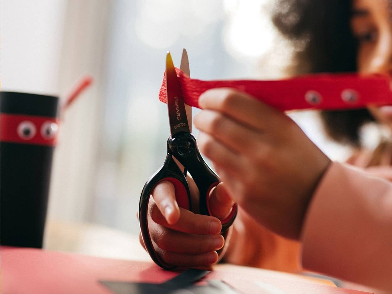 Una bambina usa delle forbici Fiskars per tagliare della carta rossa.