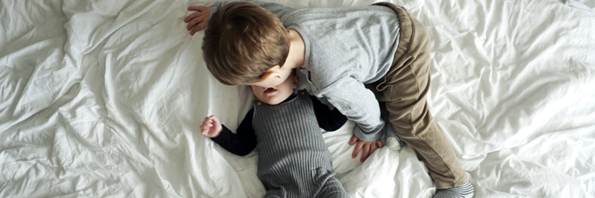 Due bambini in un letto bianco, uno abbraccia l'altro.
