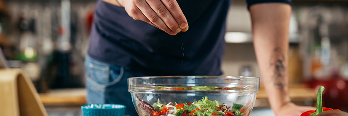 Mann würzt einen Salat mit Salz.