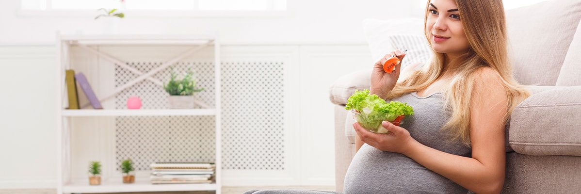Donna incinta che mangia un'insalata.