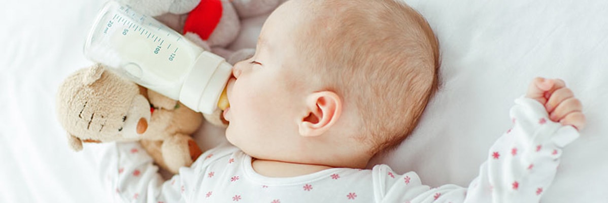Bébé dormant avec un biberon et un ours en peluche.