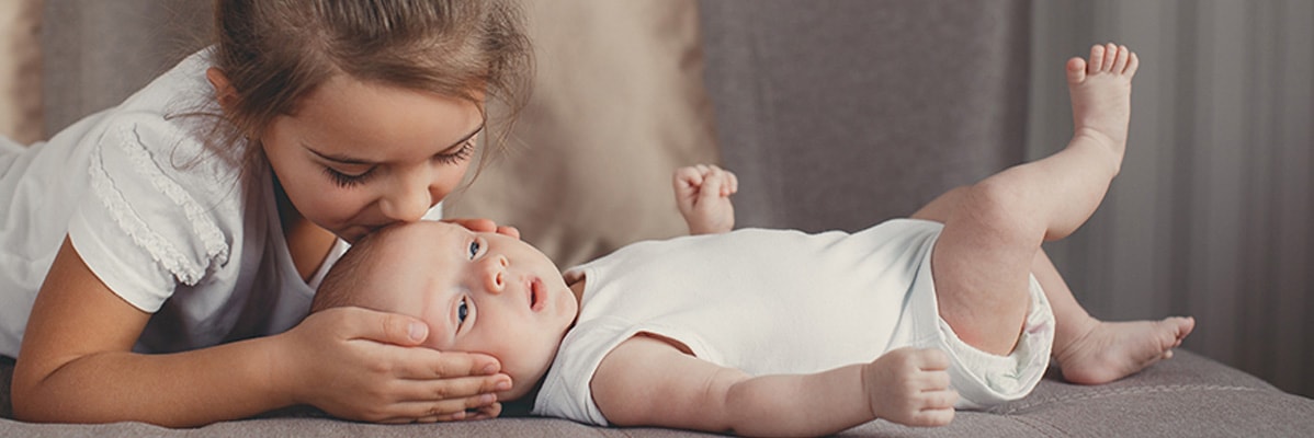 Sorella maggiore bacia un bambino vestito di bianco.
